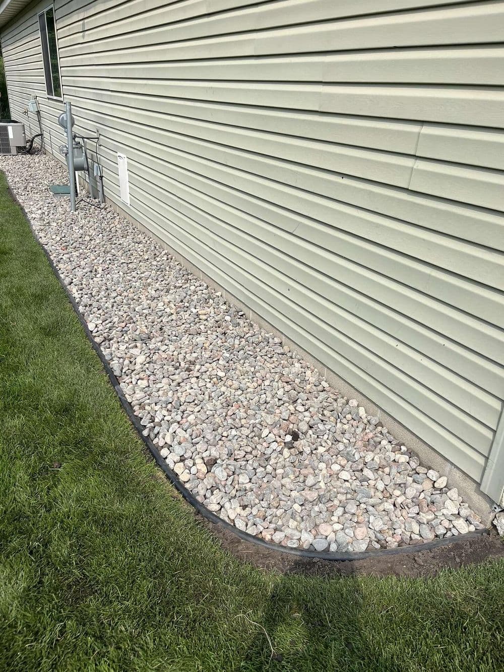Landscape feature with decorative gravel alongside a house foundation and green grass.